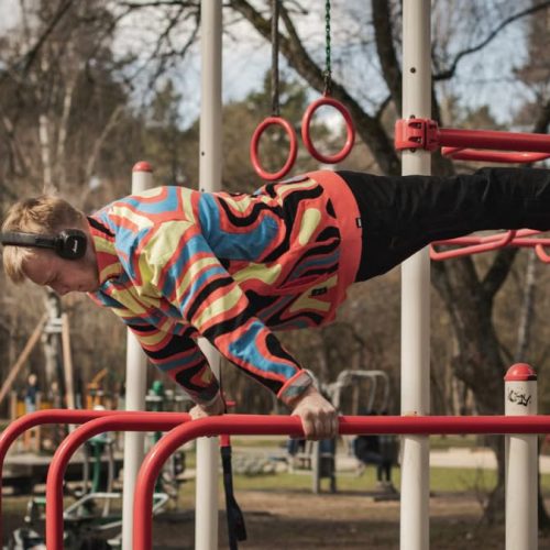 Young adult man exercises on outdoor gym bars in a colorful outfit in Vilnius, Lithuania.
